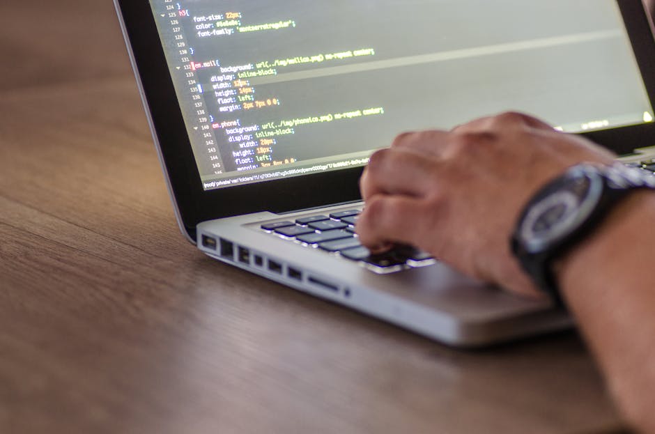 A photograph depicts a close-up view of a computer screen displaying lines of HTML code with colorful syntax highlighting, including tags, attributes, and text. The screen's background appears dark, w