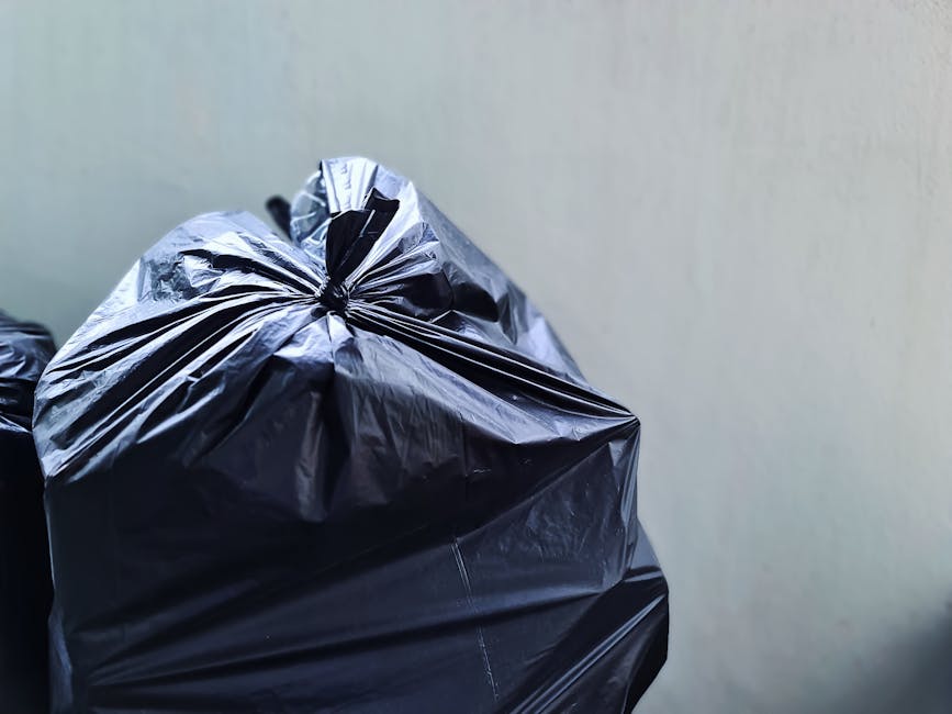 A clear disposable plastic container with a ribbed texture on the sides, sitting on a wooden surface, holding crumpled transparent plastic wrapping or packaging material. In the background, blurred ou