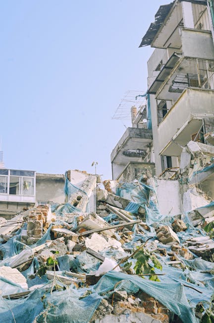 A pile of rubble and debris, consisting of broken bricks, concrete fragments, and assorted construction materials, is scattered across the ground in front of a partially damaged multi-storey residenti